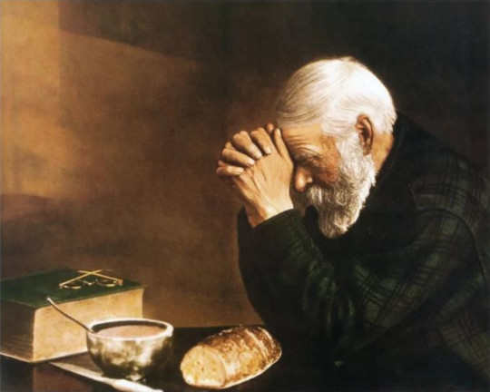 Gentleman saying grace at table adorned with Bible and food