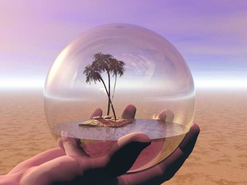 Hand holding glass globe containing an oasis with palm trees