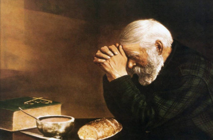 Older gentleman saying grace at table adorned with Bible and food